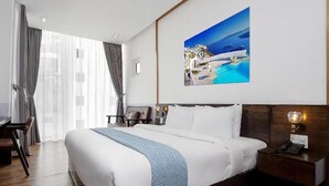 A modern hotel room with a large bed, wooden flooring, a desk, and a large window with curtains. - Sea Sand 2 Hotel (Da Nang)
