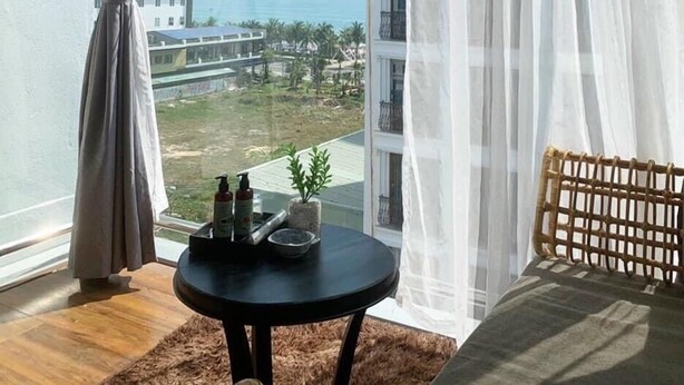 A room with a view of a cityscape and mountains. There is a round table with a bottle and a plant on it. - Sea Sand 2 Hotel (Da Nang)