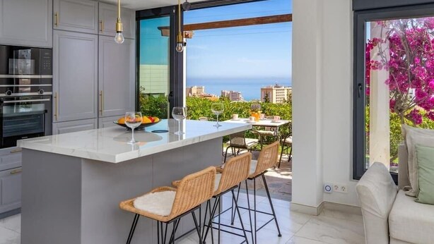 A modern kitchen with a large island, bar stools, and a view of the city and sea through large windows. - Modern Elegance/Private Pool (Fuengirola)