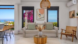 A modern living room with a sofa, a round coffee table, and a wicker chair. There is a large window with a view of the sea. - Modern Elegance/Private Pool (Fuengirola)