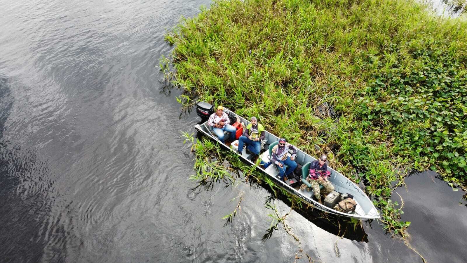 Un bote con cuatro personas, parcialmente sumergido en el agua cerca de una orilla cubierta de hierba.