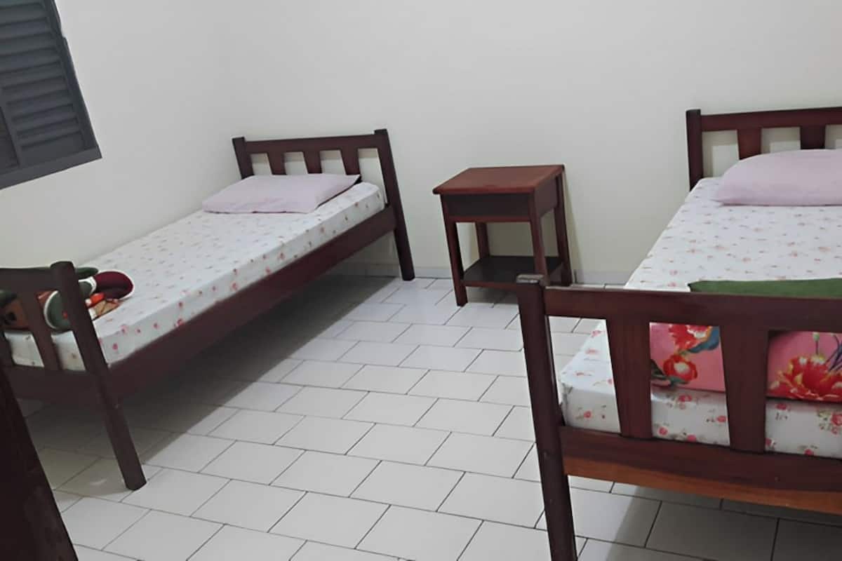 A small, clean room with two single beds, a small table, and a chair.