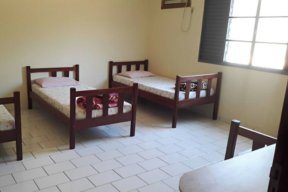 A dormitory room with three wooden beds, a desk, and a chair.
