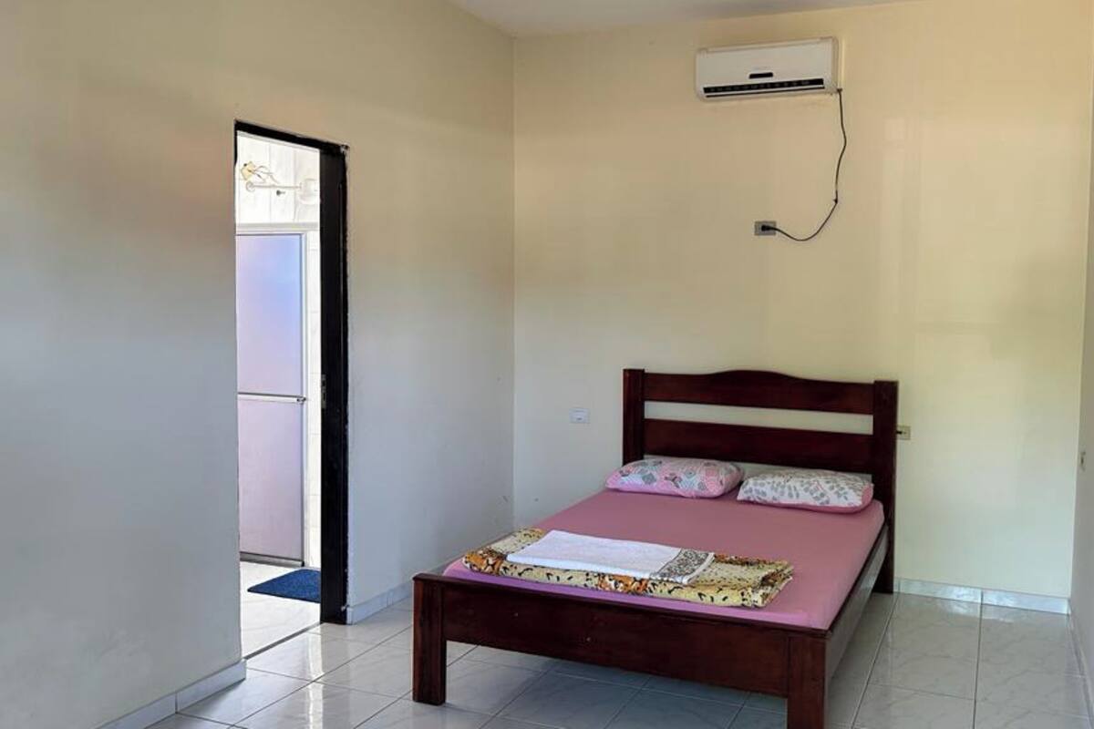 A small, clean room with a single bed, a door, and an air conditioning unit on the wall.