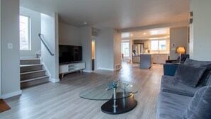 A modern living room with a flat-screen TV, a glass coffee table, and a gray sofa.