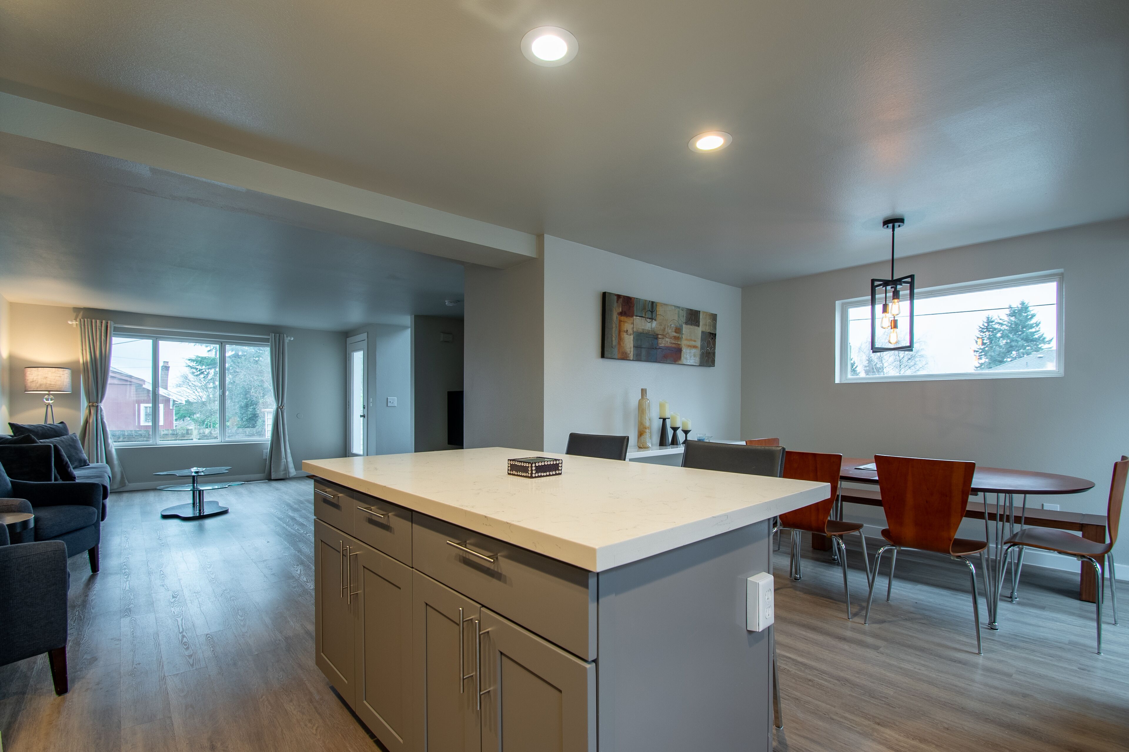 A modern kitchen with a central island, dining area with chairs, and a large window providing natural light.