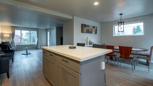 A modern kitchen with a central island, dining area with chairs, and a large window providing natural light.