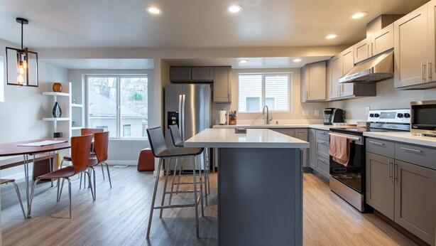 A modern kitchen with a central island, stainless steel appliances, and a dining area with bar stools.