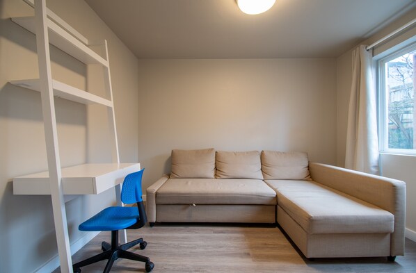 Una habitación con un sofá color beige, una silla de escritorio azul y estanterías blancas.