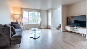 A modern living room with a sofa, glass coffee table, and a flat-screen TV on a white stand.