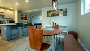 A modern kitchen with a dining area, featuring a central island, bar stools, and a pendant light.