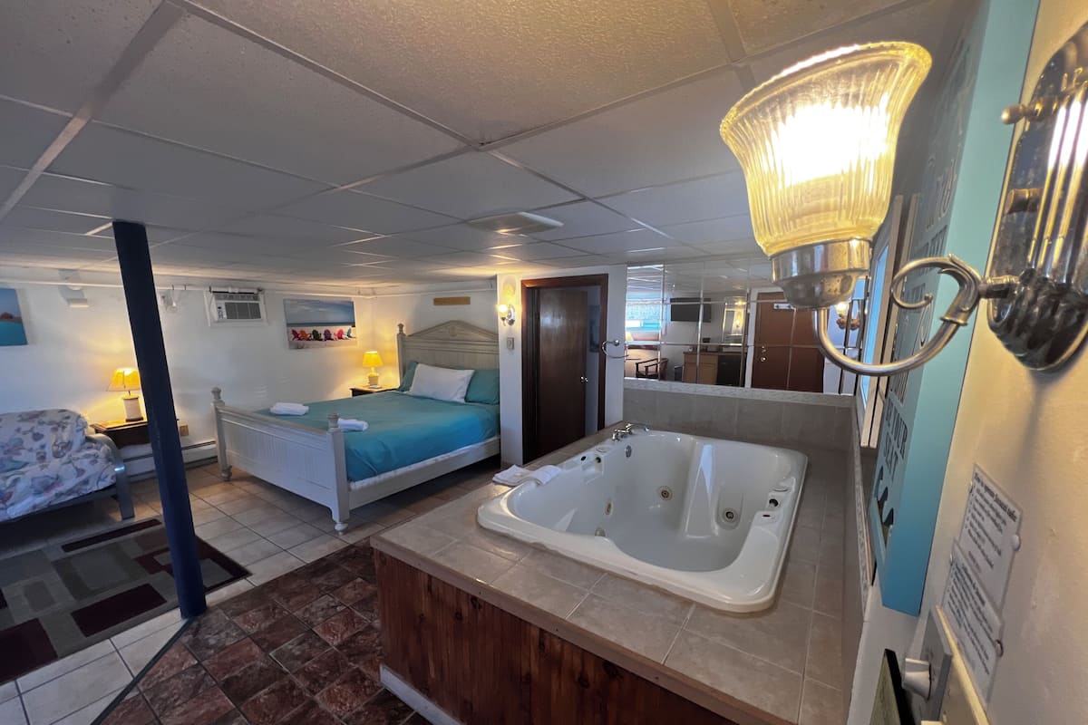 A bedroom with a bed, a bathroom with a bathtub, and a small sitting area with a chair and table.