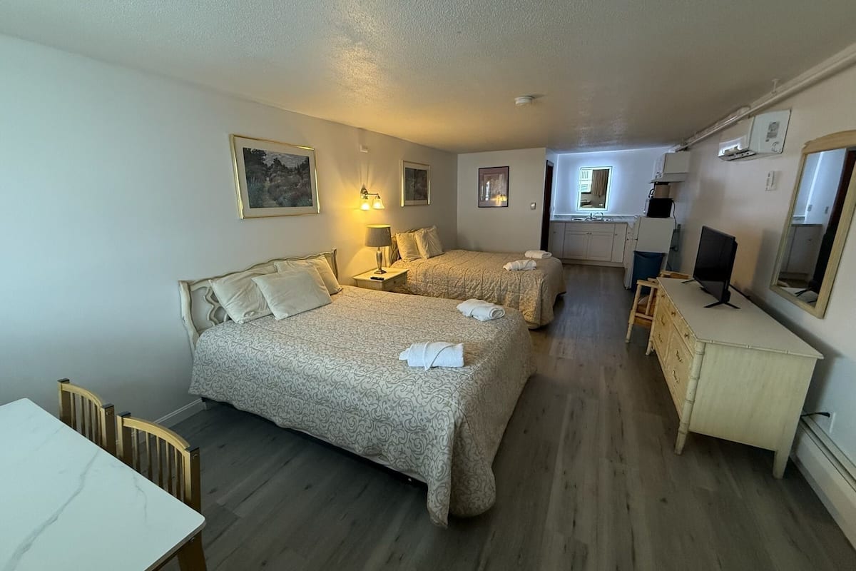 A hotel room with two beds, a desk, a dresser, and a bathroom visible through an open door.