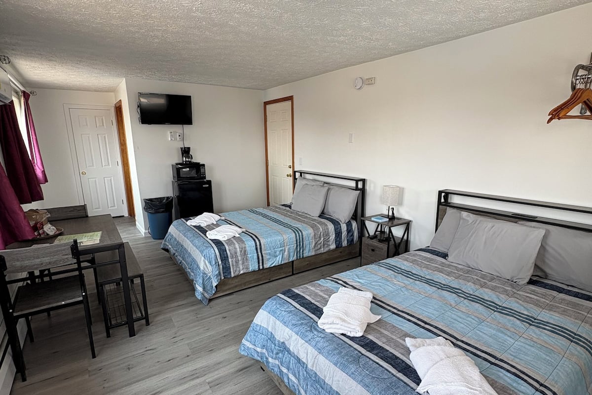 A room with two beds, a desk, a chair, a TV, and a door.