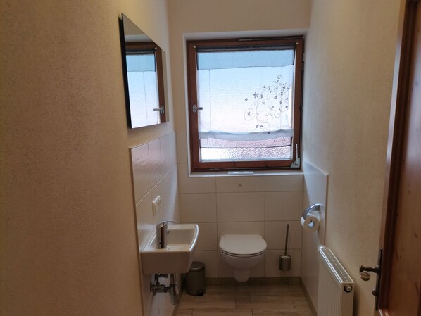 A small bathroom with a window, a sink, a toilet, and a radiator. - Ferienwohnung für 2 bis 4 Personen, 2 Schlafzimmer, Balkon, 64 m² (Inzell)