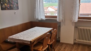 Ett litet rum med ett träbord och stolar, ett element och ett fönster med gardiner.
