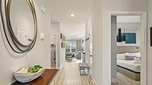 Un couloir d’hôtel avec un banc en bois, un grand miroir et un lit dans la chambre adjacente.