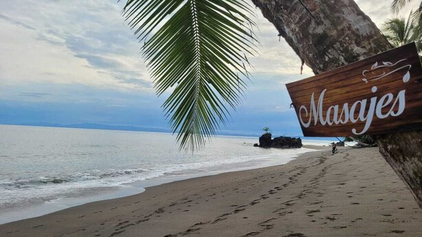 Una playa con huellas que conducen a un letrero de madera que dice "Masajes".