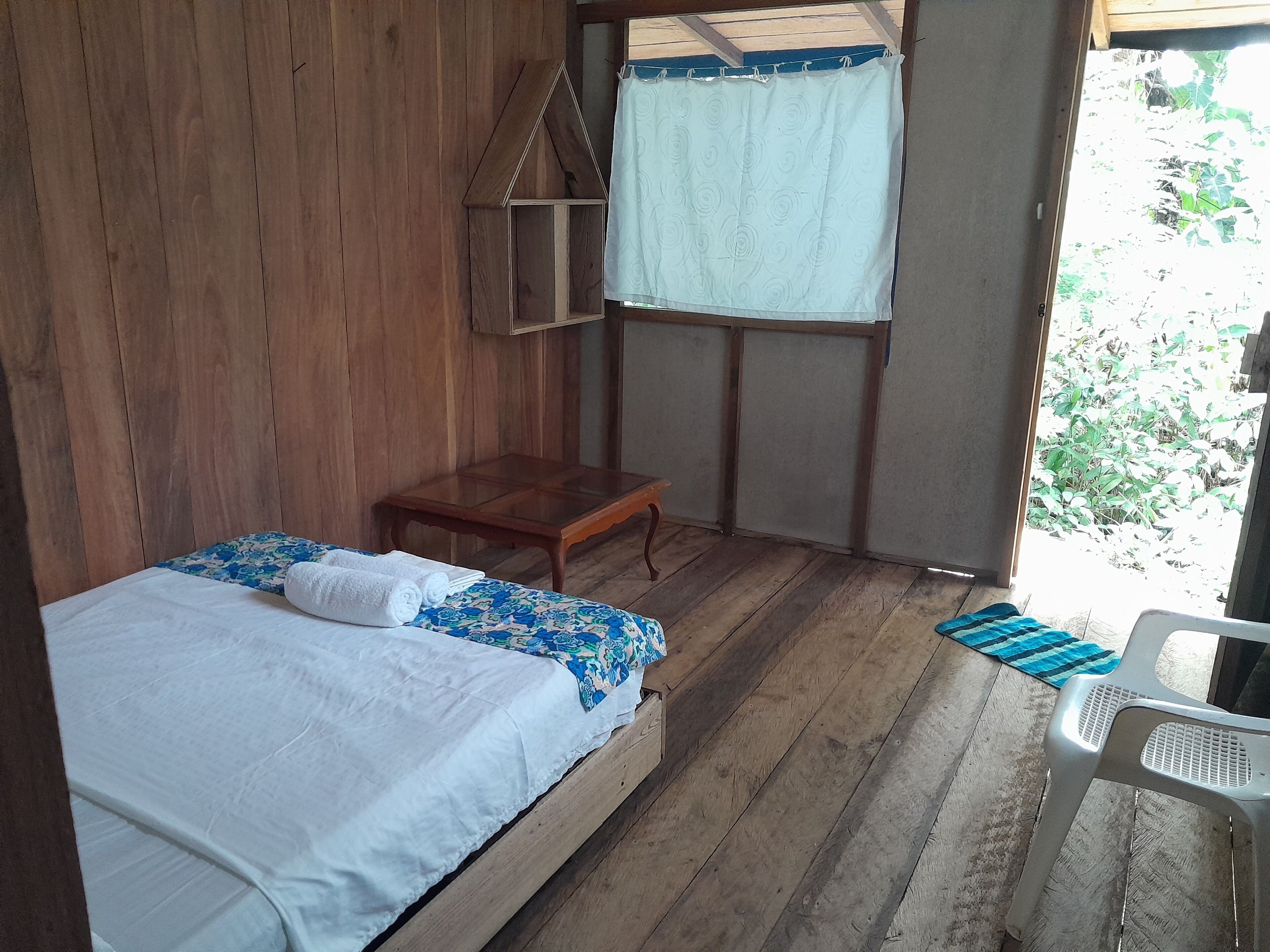 A wooden room with a bed, a small table, and a window with a curtain.