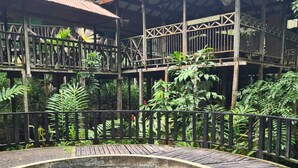 Una terraza de madera con una piscina cristalina, rodeada de exuberante vegetación y estructuras de madera con barandillas.
