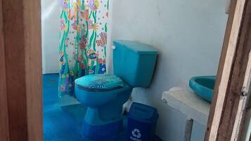 Un baño con inodoro, un cubo de basura azul, lavamanos y cortina de ducha.
