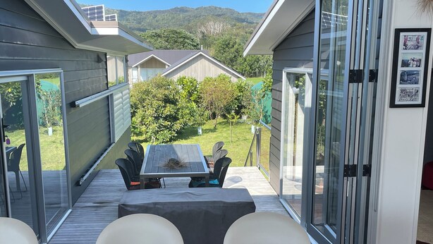 A patio area with a table and chairs, a glass door leading outside, and a framed photo on the wall. - Just ONE Minute TO Medlands Beach (Auckland)