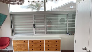 A room with a large window, a wooden cabinet with drawers, a red chair, and a white wardrobe. - Just ONE Minute TO Medlands Beach (Auckland)