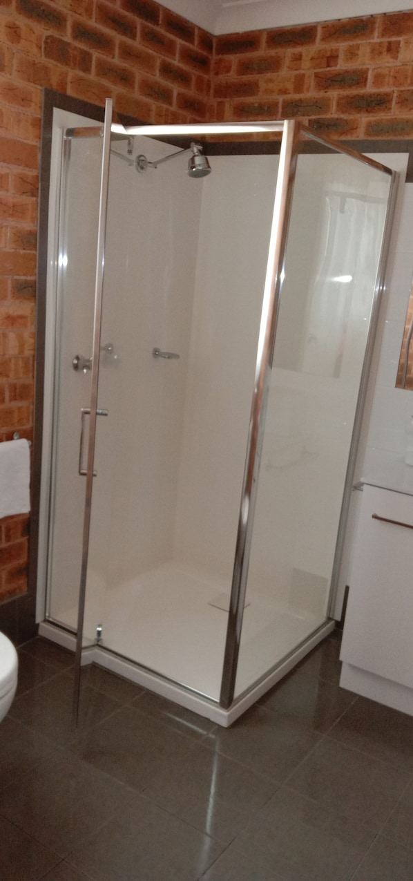 A glass-enclosed shower area with a white tiled floor, adjacent to a white toilet and a white cabinet. - The Lydoun Motel (Chiltern)