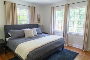 A bedroom with a large bed, two bedside tables, a nightstand, and a window with curtains.
