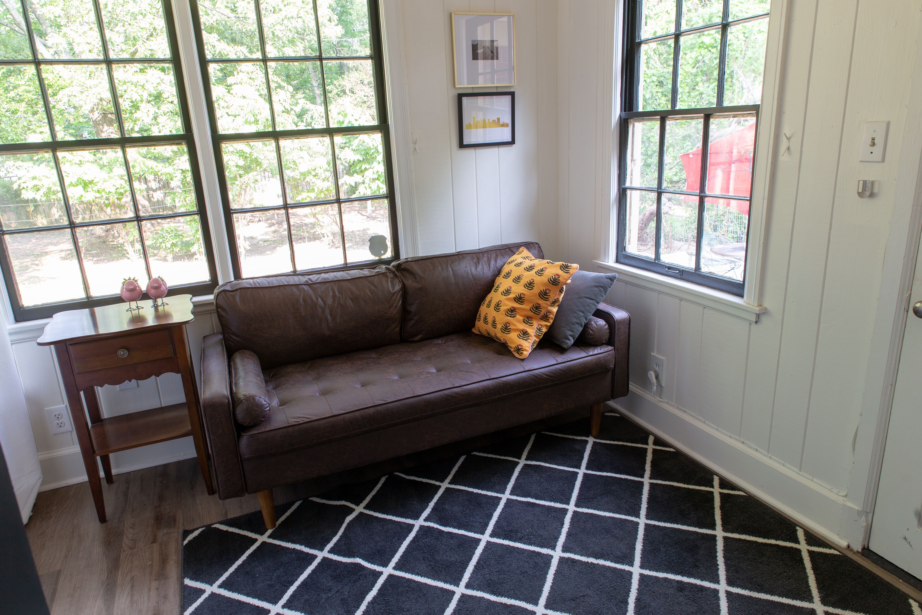 A brown leather sofa with a patterned cushion, a small wooden side table, and a black and white checkered rug.