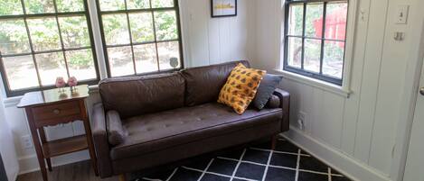 A brown leather sofa with a patterned cushion, a small wooden side table, and a black and white checkered rug.