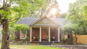 A single-story house with a front porch, a brick facade, and a front yard with a tree and a wooden fence. - J Birds' Cottage in the heart of Midtown  (Memphis)