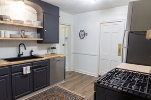 A kitchen with dark cabinets, a wooden countertop, a sink, a stove, and a door with a light switch.