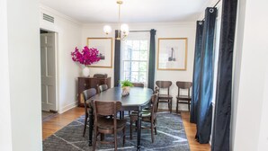 A dining area with a large table, chairs, a chandelier, and a window with curtains. - J Birds' Cottage in the heart of Midtown  (Memphis)