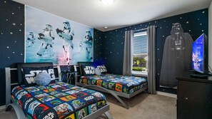 Une chambre à coucher avec du linge de lit sur le thème de Star Wars, une affiche de Star Wars et une figurine de Dark Vador.