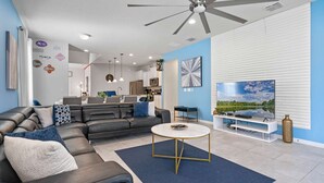 A modern living room with a black leather sofa, a round coffee table, and a TV on a white stand. - Fabulous 7 bed pool home, gated community with FREE ACCESS to resort facilities! (Kissimmee)