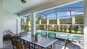 A covered patio with a pool, outdoor seating, and a view of a fenced garden. - Fabulous 7 bed pool home, gated community with FREE ACCESS to resort facilities! (Kissimmee)