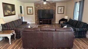 A living room with a brown leather sofa, a striped sofa, a TV, and a ceiling fan. - Alice’s Acres (Valley Head)