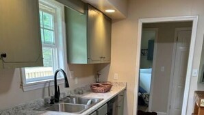 A kitchen with light green cabinets, a granite countertop, a double sink, and wooden flooring. - Alice’s Acres (Valley Head)