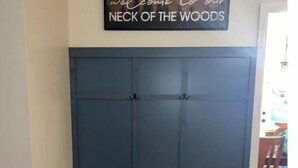 A room with a blue wardrobe, a striped bench, and a sign above the wardrobe that reads "welcome to our NECK OF THE WOODS". - Alice’s Acres (Valley Head)