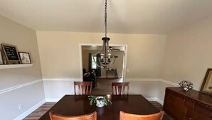 A dining room with a dark wooden table and chairs, a chandelier, and a wooden cabinet. - Alice’s Acres (Valley Head)