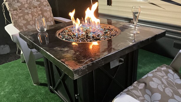 Une table avec foyer intégré, dotée d’un plateau en verre, entourée de deux chaises avec des coussins à motifs.