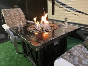 Une table avec foyer intégré, dotée d’un plateau en verre, entourée de deux chaises avec des coussins à motifs.