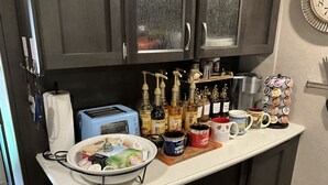 Un comptoir de cuisine avec un grille-pain, un bol de collations, une machine à café et diverses bouteilles et tasses.