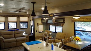 Un espace de vie compact comprenant un coin cuisine, une table à manger avec des chaises, un canapé et un ventilateur de plafond.