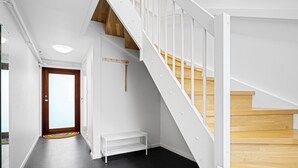 Un escalier moderne avec des marches en bois et des rampes blanches, un banc et une porte dotée d’un panneau de verre.