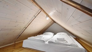 Une petite pièce avec un toit en pente, un plancher en bois et un lit recouvert de draps blancs.