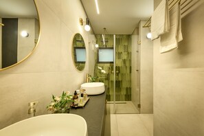 Een moderne badkamer met een grote ovale spiegel, twee wastafels, een douchecabine van glas en een meubel met toiletartikelen.
