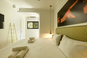 Habitación de hotel con una cama bien hecha, una escalera, un cuadro en la pared y un ventanal grande.