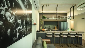 A modern kitchen with bar stools, a dining area with a sofa, and a large black and white photograph on the wall. - Sophisticated Tel Aviv Retreat 1BR Apt (Tel Aviv)